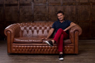 Duygu ise az ve öz odada olmak ve şişmiş kanepede oturan memnun ve gülümseyen pozitif orta yaşlı adam