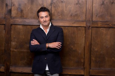 Sakin ol sana ahşap duvara yaslanmış ve kollarını sahip bakmak şık elbiseli çekici koyu saçlı adam geçti