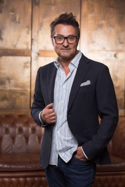 Az ve öz fotoğraf arka plan üzerinde kahverengi kanepe ile ayakta ve sana gülümseyen süre bakmak emin iş adamı