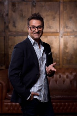 Arkasından kahverengi kanepe ile ayakta ve bir fotoğraf için poz hareketleri kullanarak duygusal mutlu adam