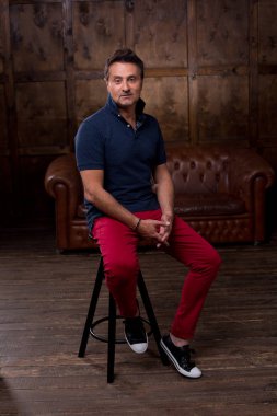 Barda oturan rahat kıyafetler düşünceli orta yaşlı adam tabure az ve öz odaya ve sakin seyir