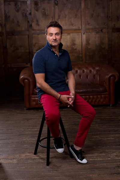 Barda oturan rahat kıyafetler düşünceli orta yaşlı adam tabure az ve öz odaya ve sakin seyir