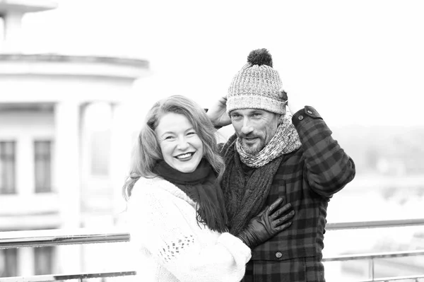 Couple in love. Guy in hat and blonde hair girl. Happy woman hugs man. Man dressing on hat and smiling woman with woolen scarf. Happy couple meet in town.