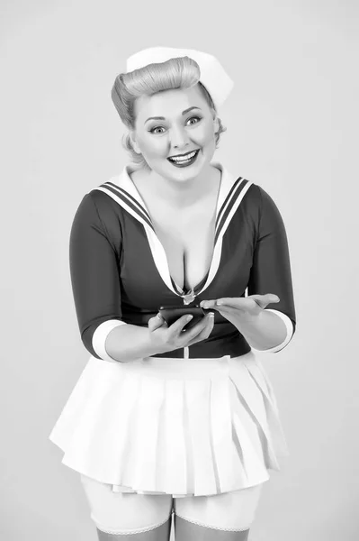 Excited cheerful lovely blonde girl got sms on smartphone. Girl typing messages to her friend. Lady with telephone on gray background. Pin-up styled lady emotionally received sms. She got a message!
