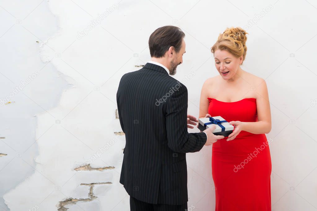 So pleasant. Charming adorable woman wearing red trendy dress and expressing amusement while receiving birthday present from her positive husband