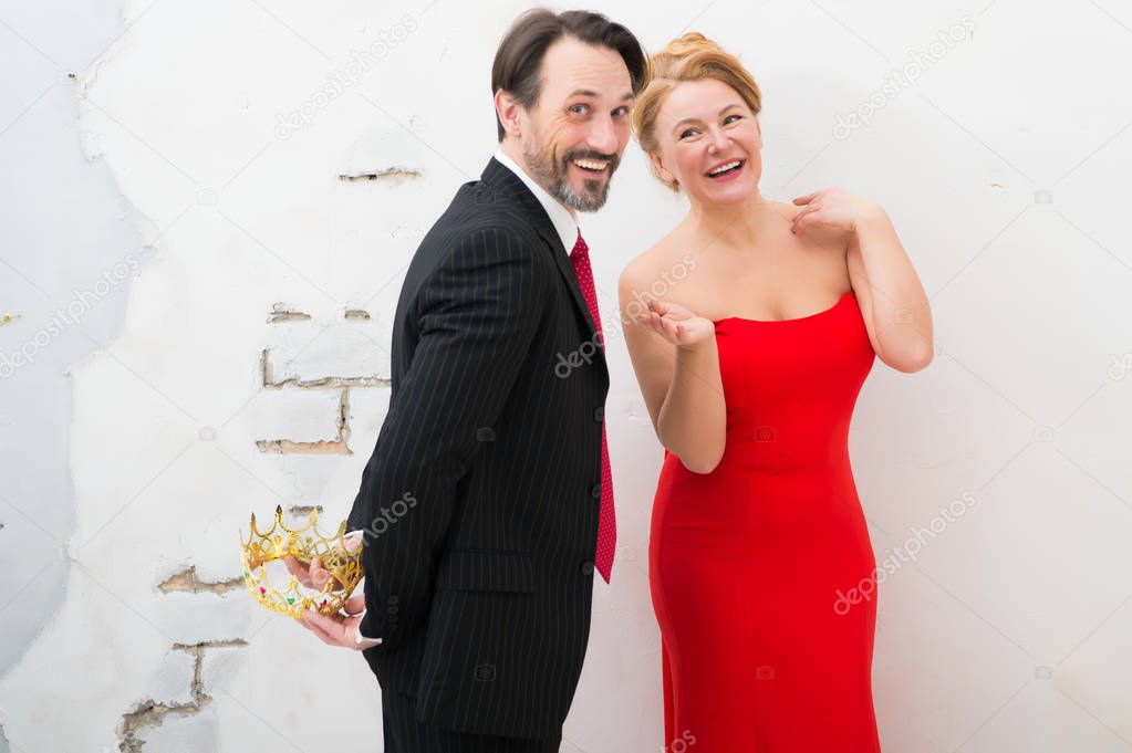 Splendid mood. Smiling bearded man holding golden crown behind his back and making surprise while his pretty joyful wife waving hands and feeling entertained