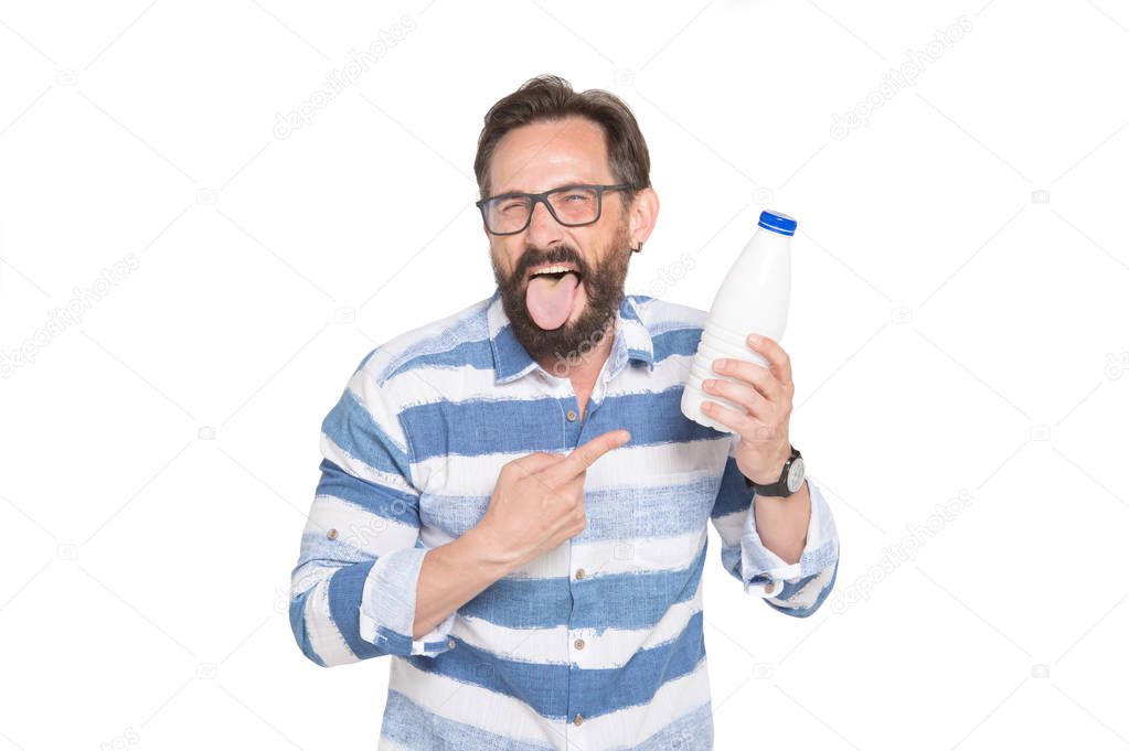 What a nasty drink. Nervous bearded man wearing spectacles and keeping his tongue out while holding a bottle of milk and expressing disgust