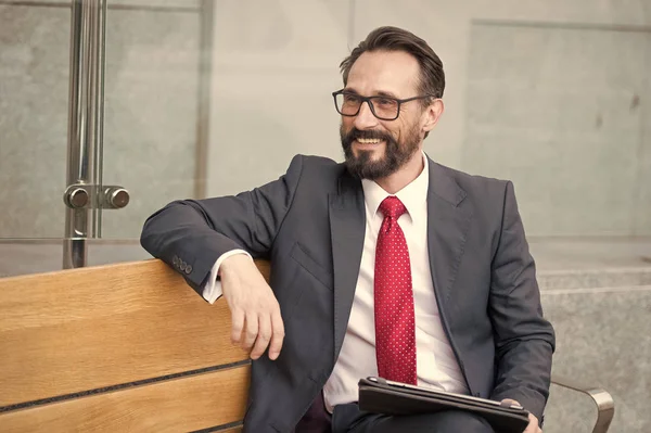 Negócios, Lazer, tecnologia, comunicação e conceito de pessoas. Retrato de belo homem sorridente de terno relaxante ao ar livre no banco usando seu tablet digital — Fotografia de Stock