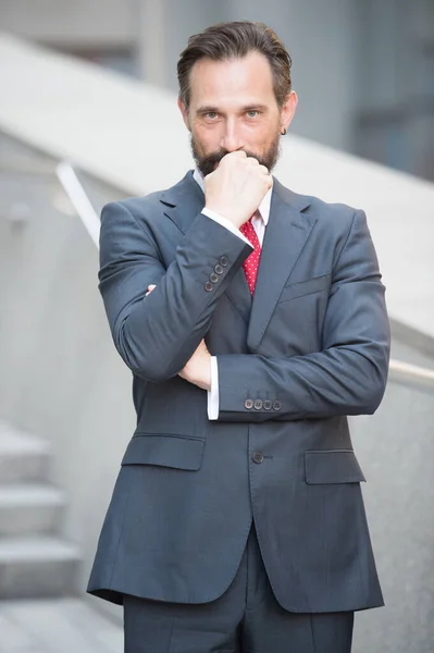 Pensive businessman looking at you with his fist near chin