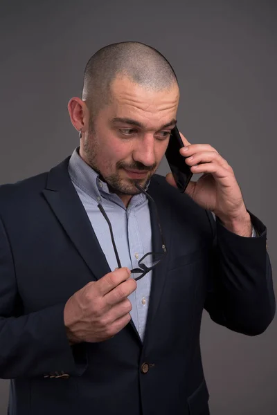 Empresario reflexivo hablando en el teléfono móvil mientras mantiene hola —  Fotos de Stock