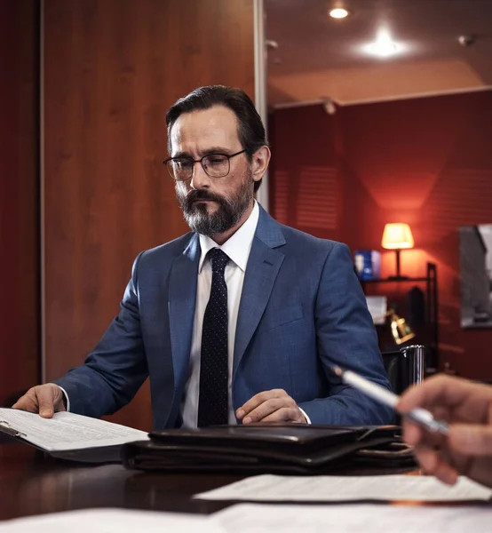 Signing papers. Serious bearded man in white shirt, tie and jacket filling documents while sitting in the office — Stock Photo, Image