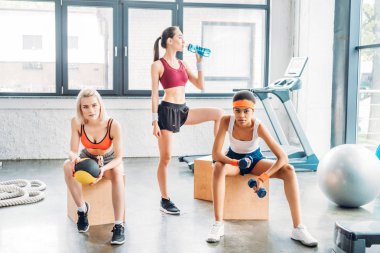 Genç Asyalı sporcumuz içme suyu süre egzersiz ve spor salonunda ahşap kutular üzerinde oturan iki kadın sporcular