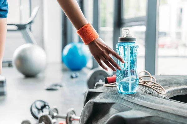 腕带上运动员的裁剪图像在健身房训练轮胎时捡起一瓶水 — 图库照片