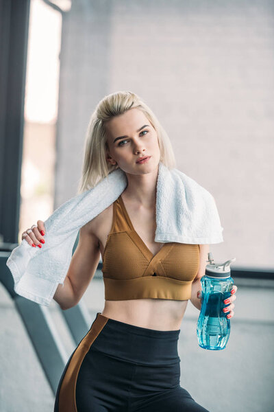 portrait of young sportswoman with sportive water bottle and towel after workout at gym