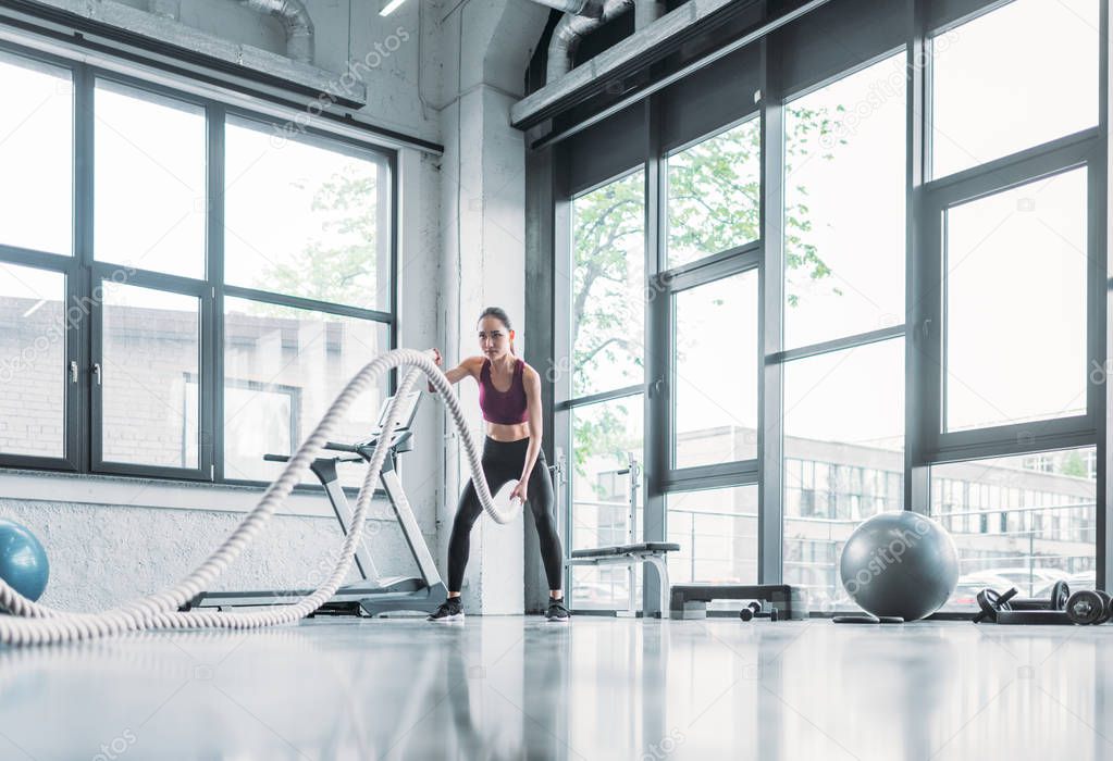 asian sportswoman working out with battle ropes at gym