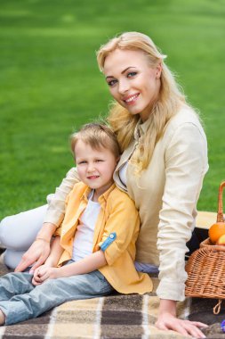 mutlu anne ve oğlu birlikte ekose piknik üzerinde otururken kameraya gülümseyen