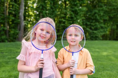 badminton raket tutarak ve kamera Park gülümseyen şirin küçük çocuklar