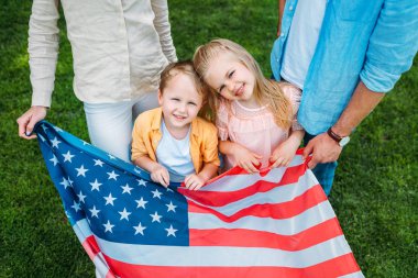cropped shot of happy family holding american flag, kids smiling at camera clipart