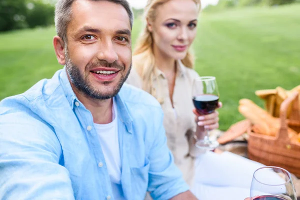 ワインのグラスを持って ピクニックにカメラで笑顔の幸せなカップルの選択と集中  — 無料ストックフォト