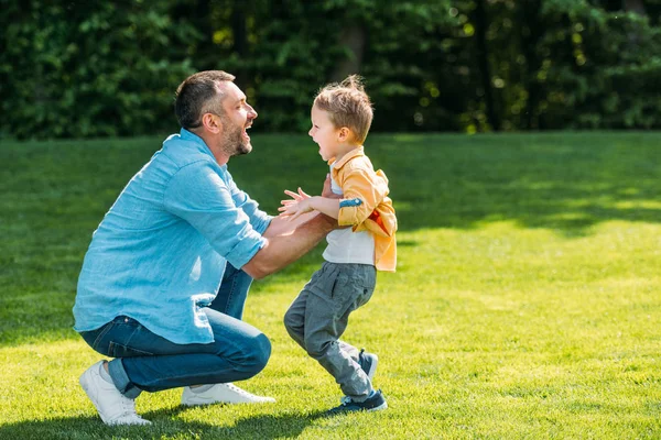 愉快的父亲和儿子的侧面看法拥抱和互相微笑在公园里 — 图库照片