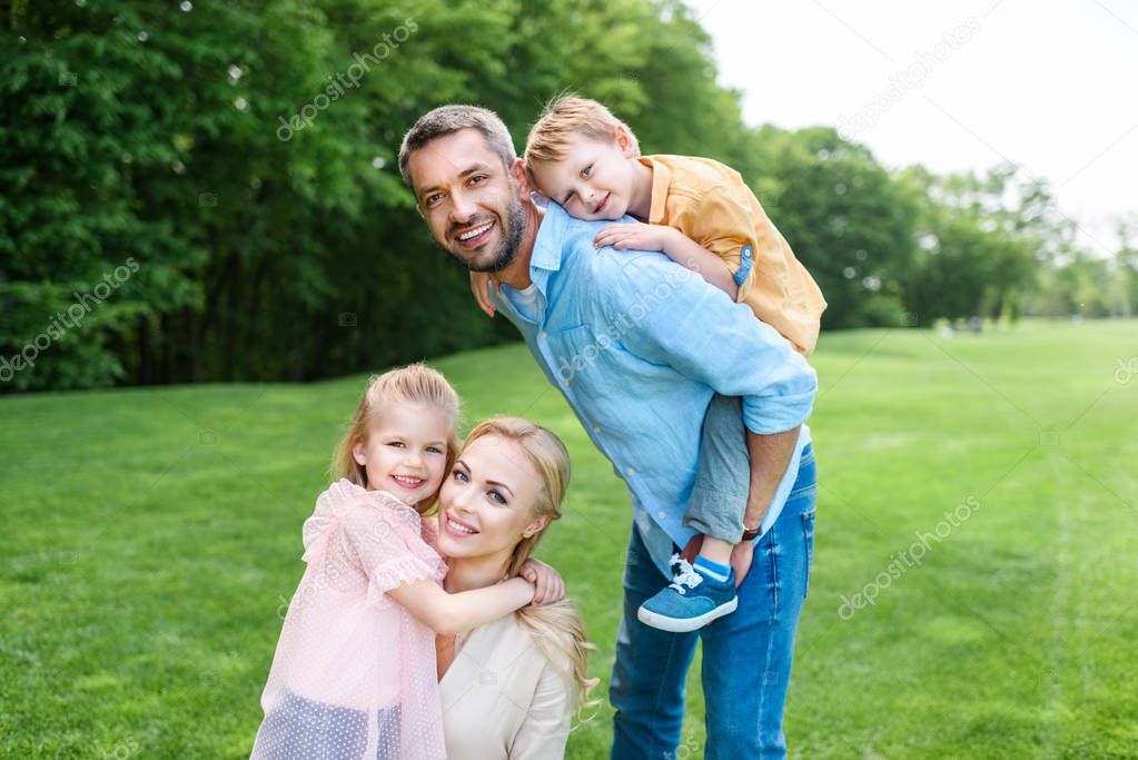 happy family with two kids smiling at camera while spending time together in park  