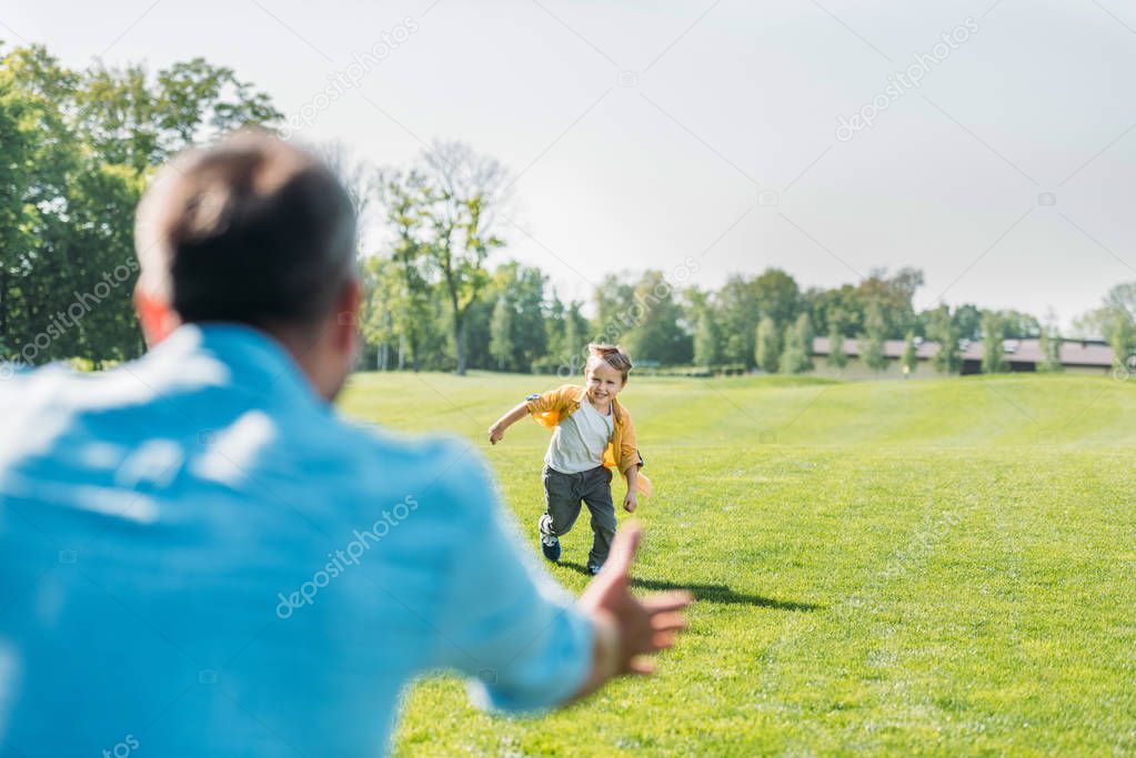 selective focus of father with open arms looking at happy little son running in park