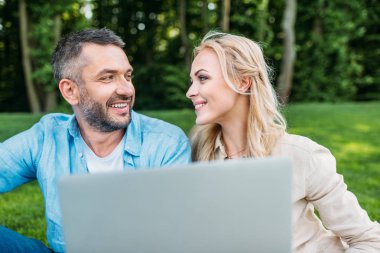 dizüstü bilgisayar kullanarak ve birbirlerine parkta gülümseyen mutlu çift