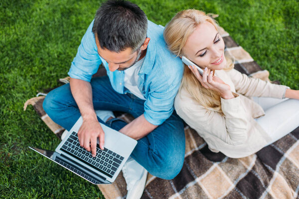 high angle view of happy couple using smartphone and laptop in park 
