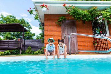 little siblings sitting near swimming pool on summer day clipart