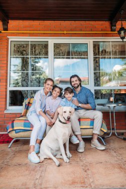 Ülke evi sundurma birlikte kanepede oturan gülümseyen aile labrador köpek 