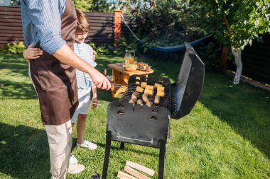 Oğlunun babası pişirme sosis ve Mısır arka bahçe Barbekü üzerinde bakarak kısmi görünümü