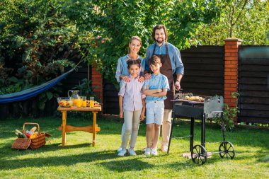 mutlu bir aile barbekü birlikte arka bahçesinde üzerinde yaz gününde yaparken kameraya bakıyor