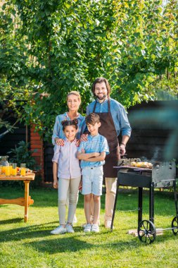 mutlu bir aile barbekü birlikte arka bahçesinde üzerinde yaz gününde yaparken kameraya bakıyor
