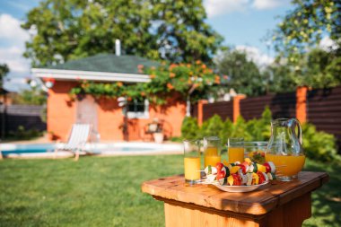 selective focus of fresh vegetables for barbecue and glasses of juice on backyard clipart