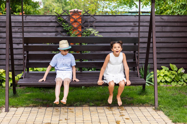 cute kids sitting on wooden bench together on backyard on summer day