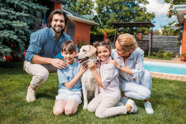 счастливая семья с собакой-лабрадором, смотрящей в камеру, проводя время на заднем дворе загородного дома в летний день
