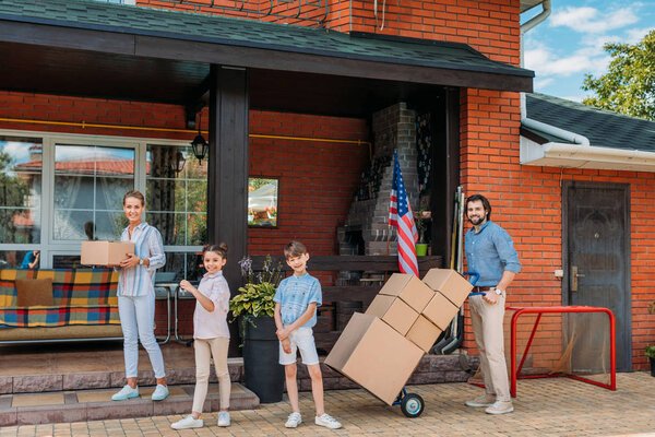 parents with cardboard boxes and children standing at country house, moving home concept