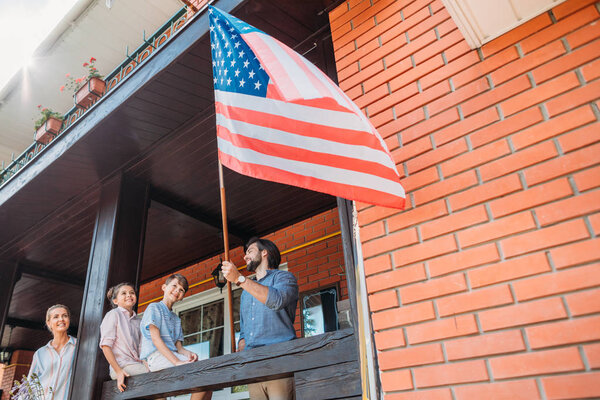 family with american flag standing on country house porch