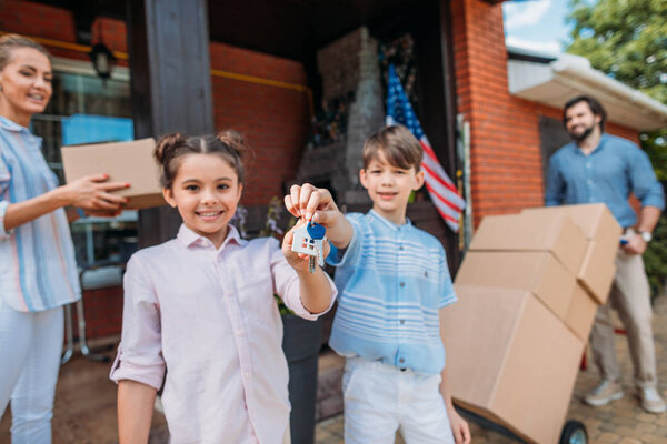 smiling children with keys and parents with cardboard boxes standing at country house, moving home concept