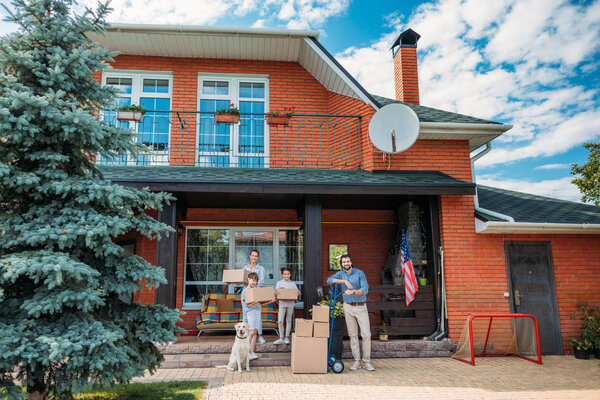 family with cardboard boxes and labrador dog standing on country house porch, moving home concept