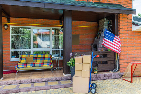 hand truck with cardboard boxes and sofa on porch of country house