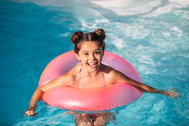 portrait of happy kid with inflatable ring swimming in swimming pool on summer day clipart