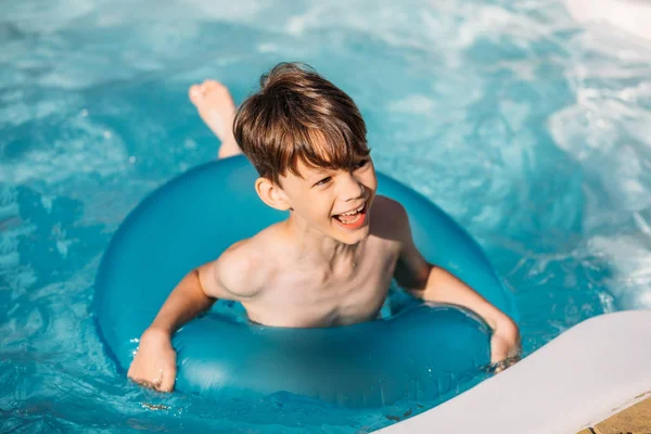 portrait of happy boy with inflatable ring swimming in swimming pool on summer day