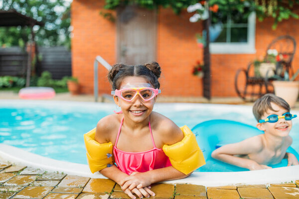 portrait of little siblings swimming in swimming pool together on summer day