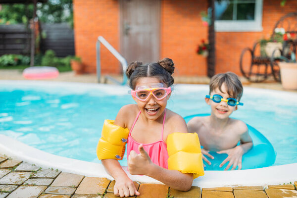 little siblings swimming in swimming pool together on summer day