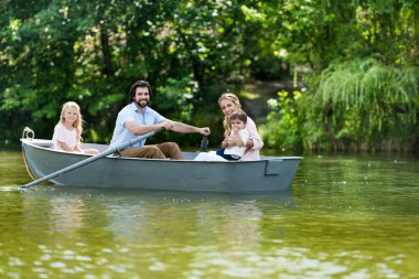 happy young family spending time together in boat on river at park and looking at camera