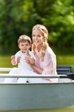 happy mother with son spending time together in boat at park clipart