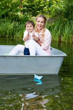 happy mother with son riding boat on lake at park and clapping hands  clipart