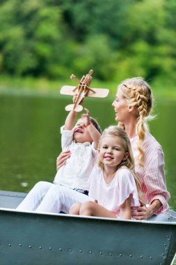 happy mother and kids riding boat on lake at park clipart