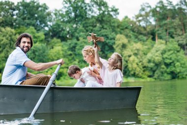 happy young family riding boat on lake at park together